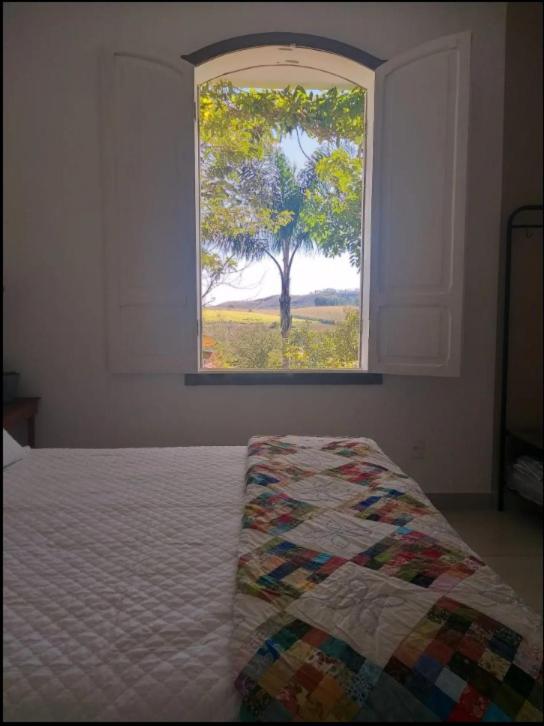 a bedroom with a bed and a window with a tree at Quinta Vogrande no bairro de Águas Santas entre Tiradentes e São João Del Rey in Tiradentes