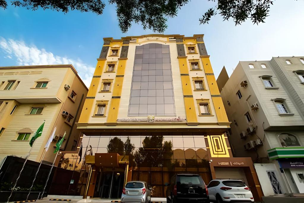 żółty budynek z samochodami zaparkowanymi przed nim w obiekcie Hayat Al Rose Hotel Appartment w mieście Dżudda