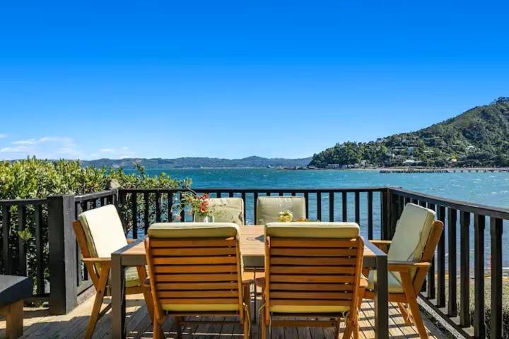 a wooden table and chairs on a balcony with the water at Seaglass Cottage in Lower Hutt
