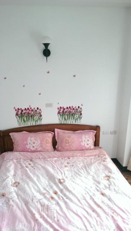 a bed with pink sheets and flowers on the wall at Cuiti B&amp;B in Fenqihu