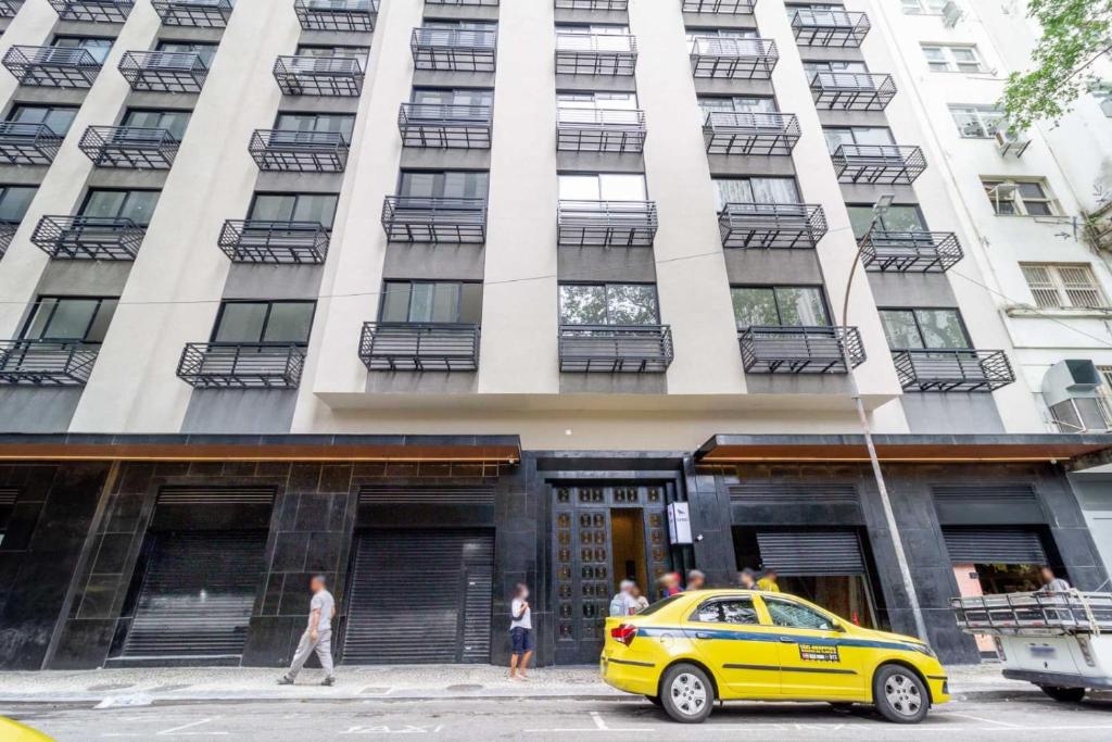 um táxi amarelo estacionado em frente a um edifício alto em Apartamento Centro/Lapa-RJ Rua Sen. Dantas n.°80 no Rio de Janeiro