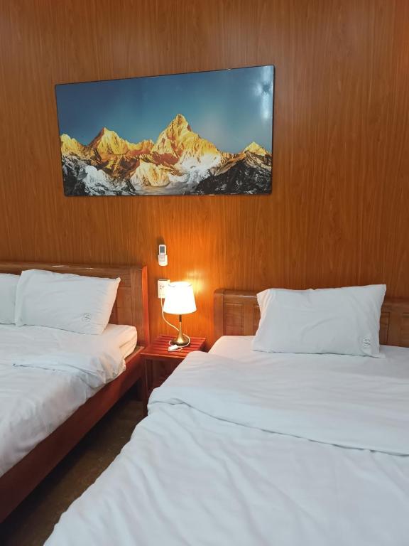 two beds in a hotel room with a picture on the wall at An Homestay & Hostel Motorbikes & Tours in Cao Bằng