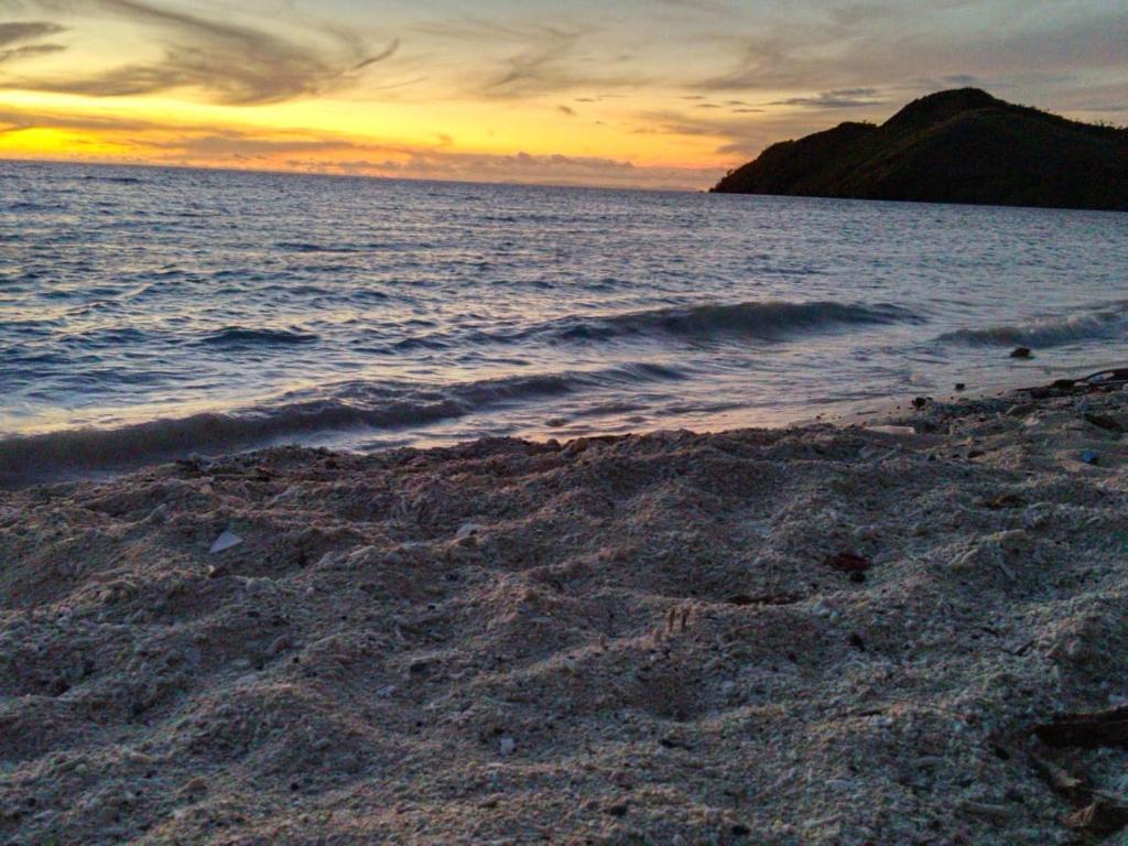 a sandy beach with a sunset in the ocean at Or Mandira Homestay in Fam