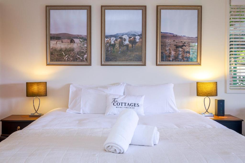 ein Schlafzimmer mit einem weißen Bett mit drei Bildern an der Wand in der Unterkunft The Cottages On Mount Tamborine in Mount Tamborine