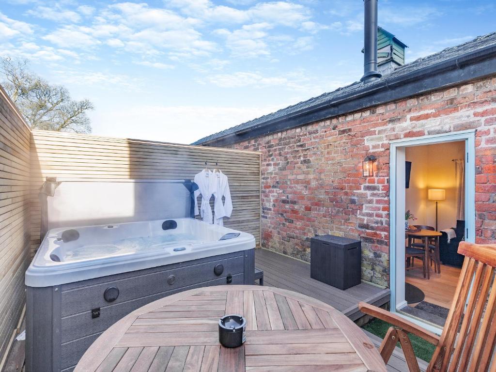 un patio con bañera de hidromasaje y mesa de madera en Rose Cottage - Uk45497 