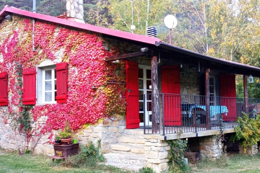a house covered in ivy with red doors and windows at Cottage a Bossolasco con piscina in Niella Belbo