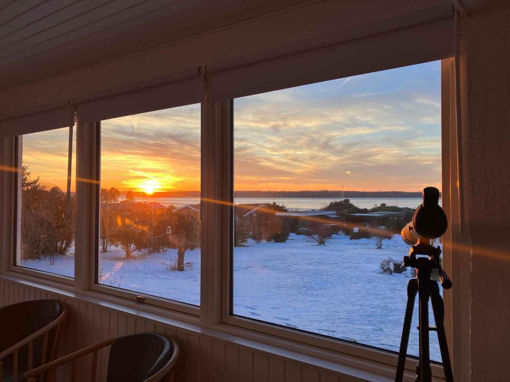 Cozy Summerhouse With Spectacular Views! في Ølsted: شخص يلتقط صورة لغروب الشمس من خلال النافذة