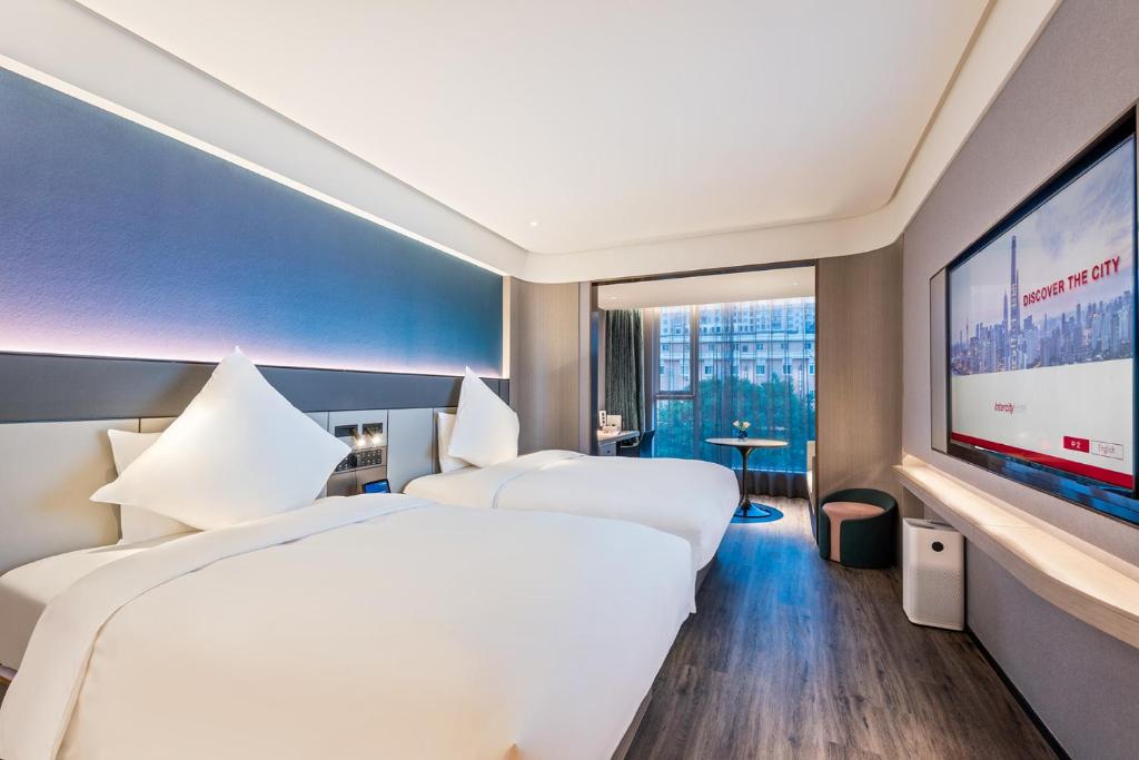 two beds in a hotel room with a flat screen tv at Intercity Yangzhou Slender West Lake in Yangzhou