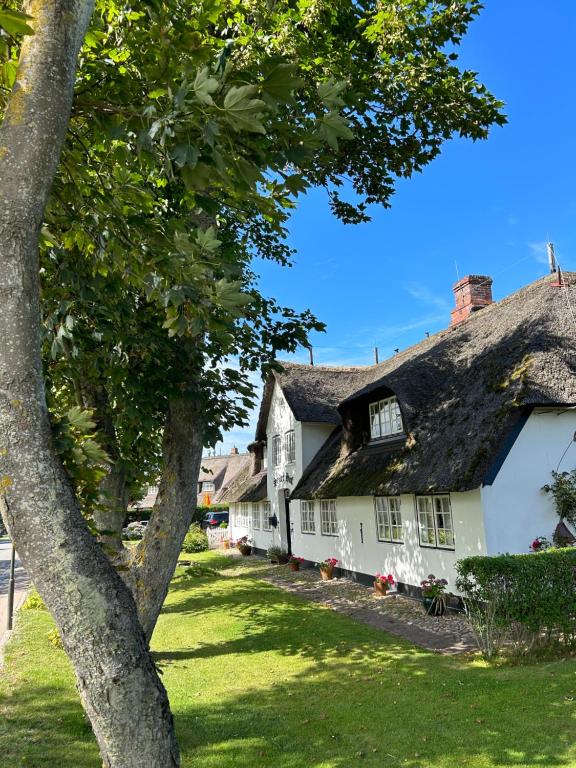 ein altes Cottage mit einem Strohdach und einem Baum in der Unterkunft Hotel Seiler Hof Keitum garni in Keitum