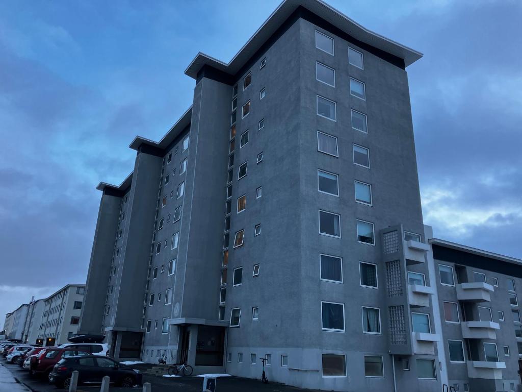 a tall gray building with cars parked in a parking lot at Private room in a shared apartment with amazing view in Reykjavík