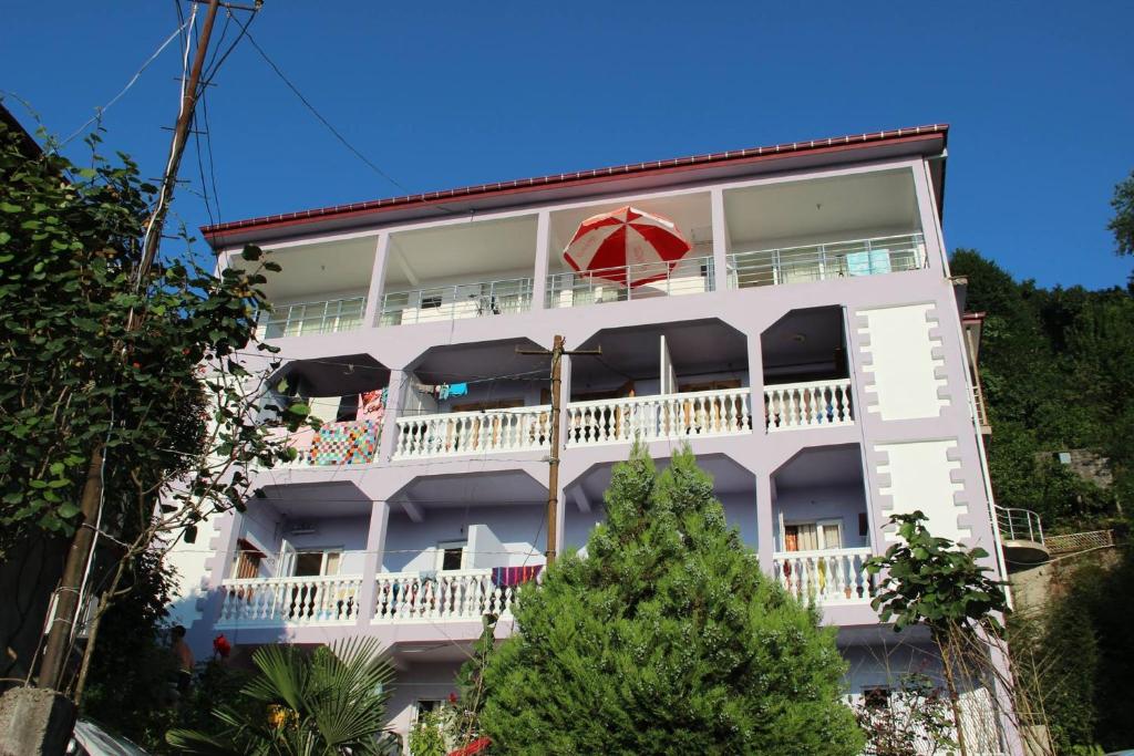 ein weißes Gebäude mit einem Balkon und einem roten Regenschirm in der Unterkunft Badu Guest House in Kwariati