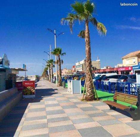 un trottoir avec des palmiers et des bancs dans une rue dans l'établissement studio cabine mer, à Port-la-Nouvelle