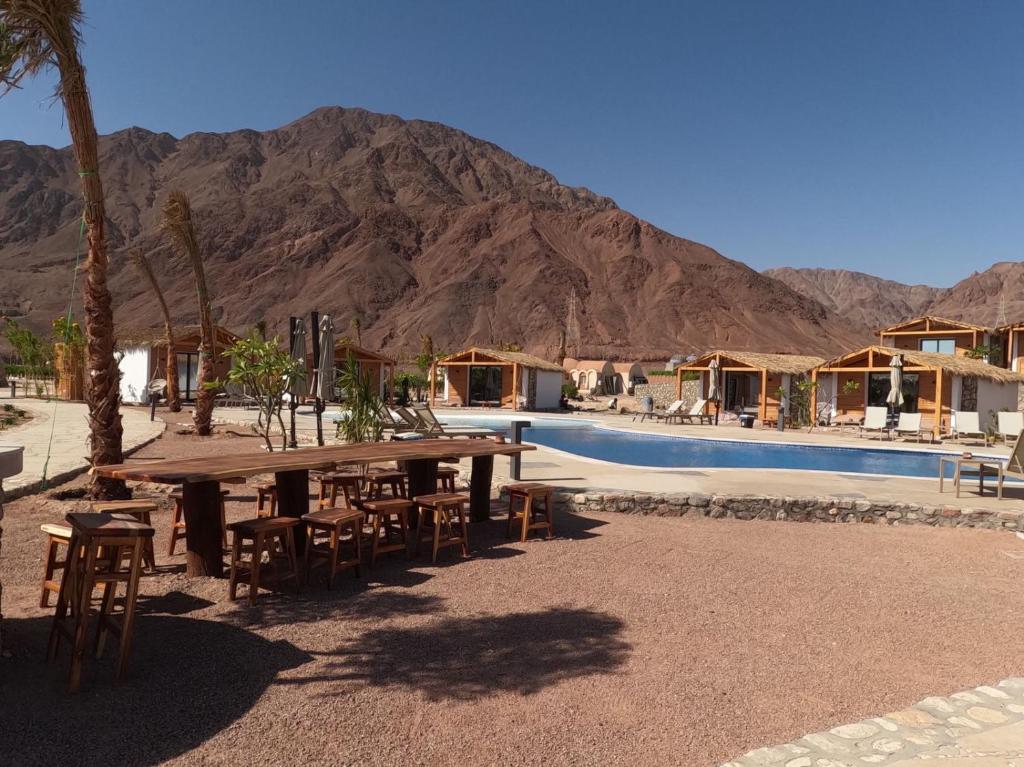 a picnic table and chairs next to a pool with a mountain at Ananda Beach Camp in Nuweiba‘ el Muzeinah