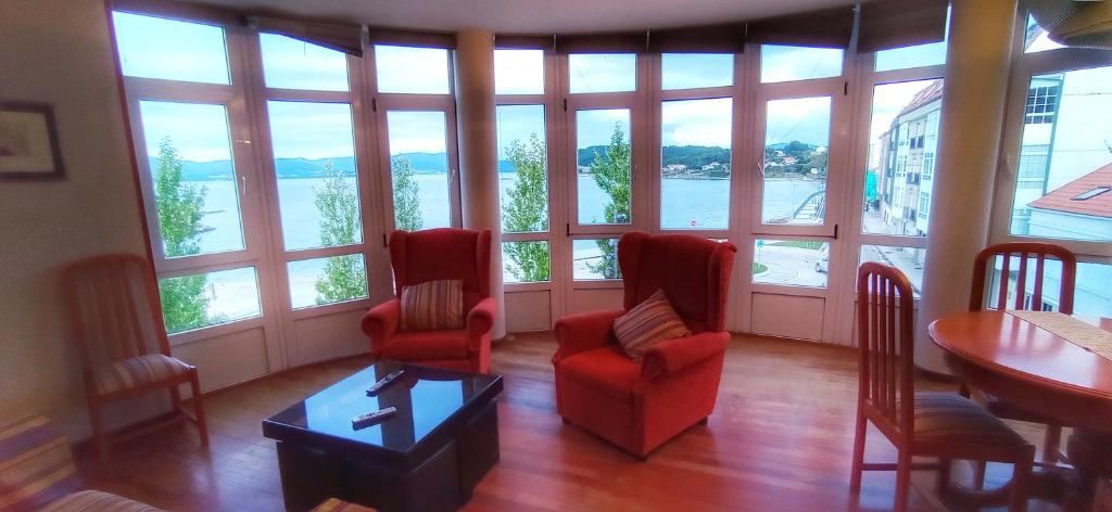 a living room with chairs and a table and large windows at Apartamento turístico en Porto do Son in Porto do Son