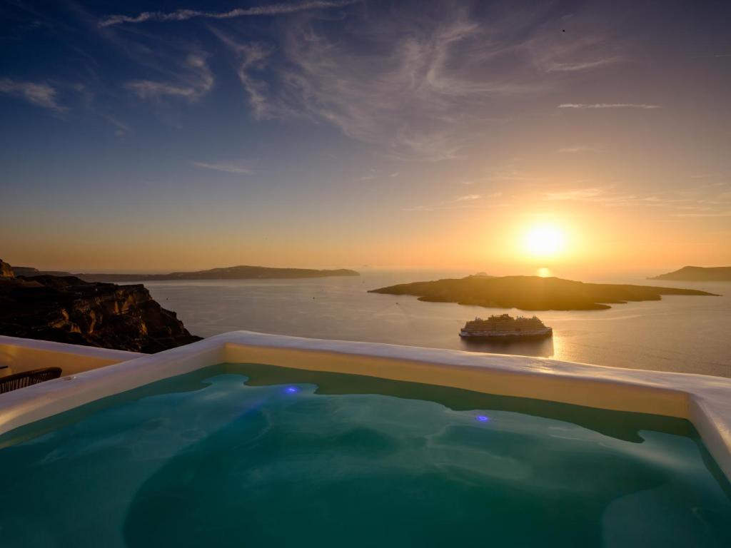 a hot tub with a view of the ocean at sunset at Kamares Apartments in Fira