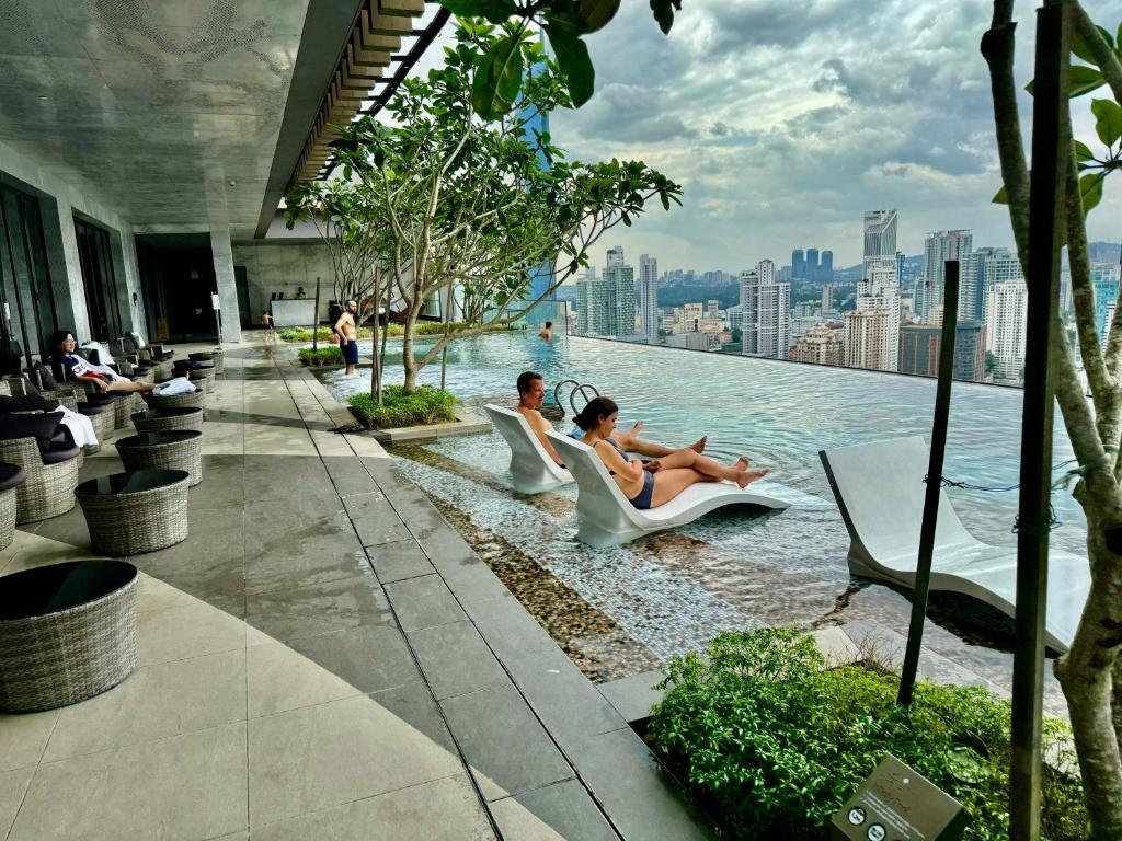 a pool with people sitting in chairs on the edge of a building at Axon Residence By Classy 1 minutes Pavilion in Kuala Lumpur