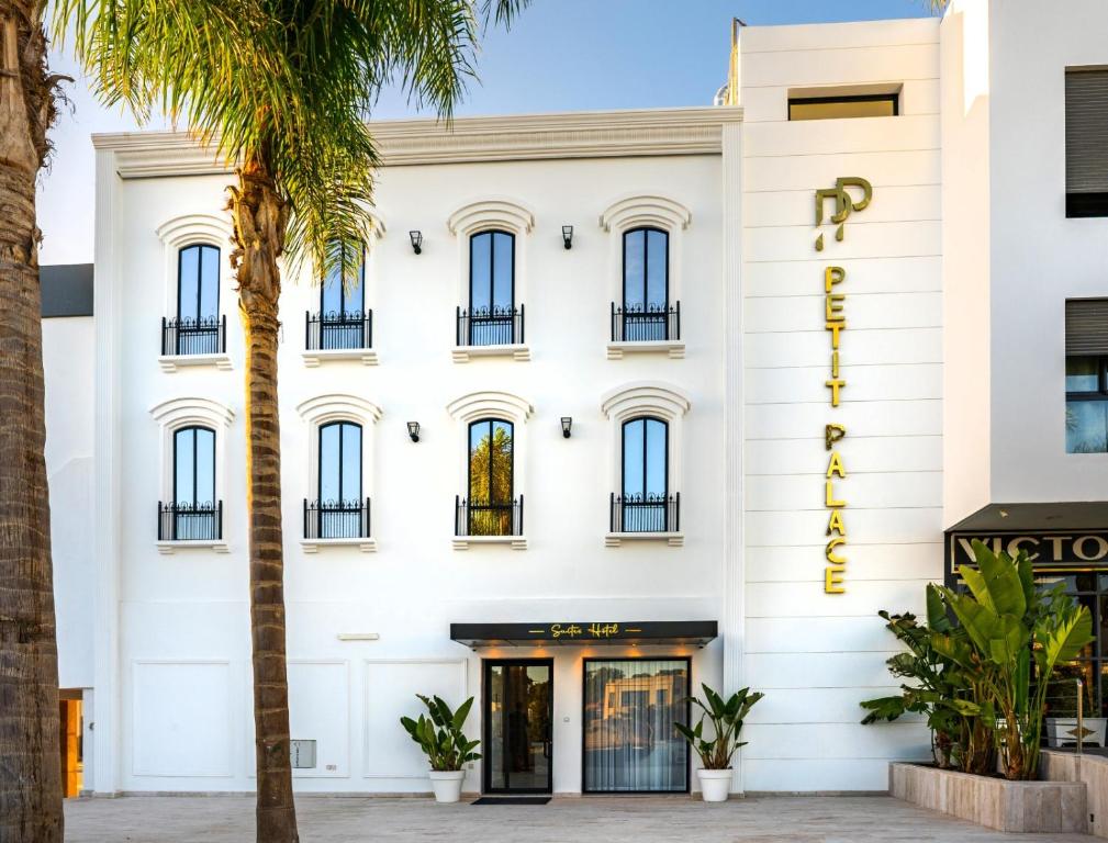 a white building with palm trees in front of it at Petit Palace Suites Hotel in Agadir