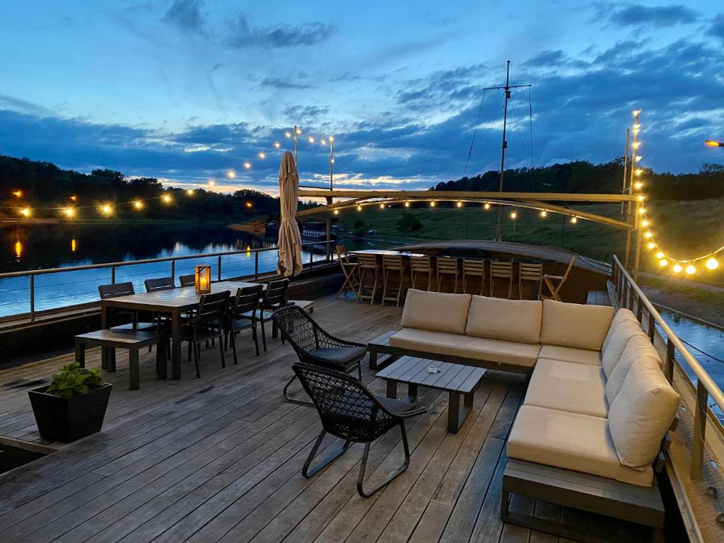 una terrazza in legno con divano, tavoli e sedie. di Tabor 67 Luxury Houseboat a Ittre