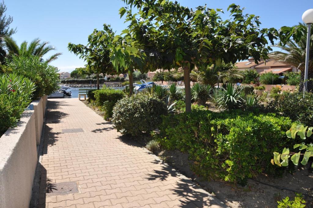 un trottoir avec des arbres et des buissons à côté d'une masse d'eau dans l'établissement Maisons du lac, au Barcarès