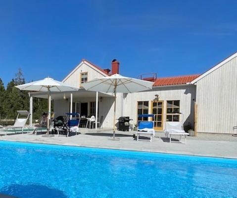 a house with a swimming pool with chairs and umbrellas at Villa VitvikenB i Gotland Pool in Slite