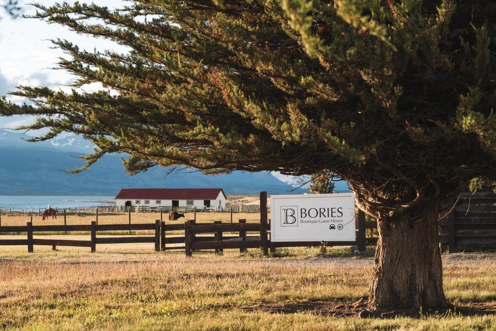 a sign in front of a tree next to a fence at Bories - Boutique Guest House in Puerto Natales