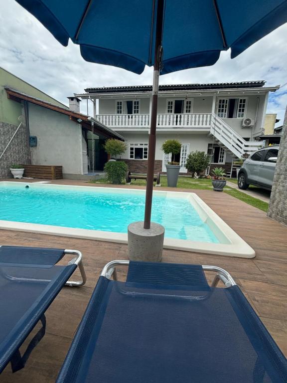 een zwembad met een parasol en twee stoelen ernaast bij Casa com piscina Balneário Camboriú CasaAlbertiBc in Balneário Camboriú