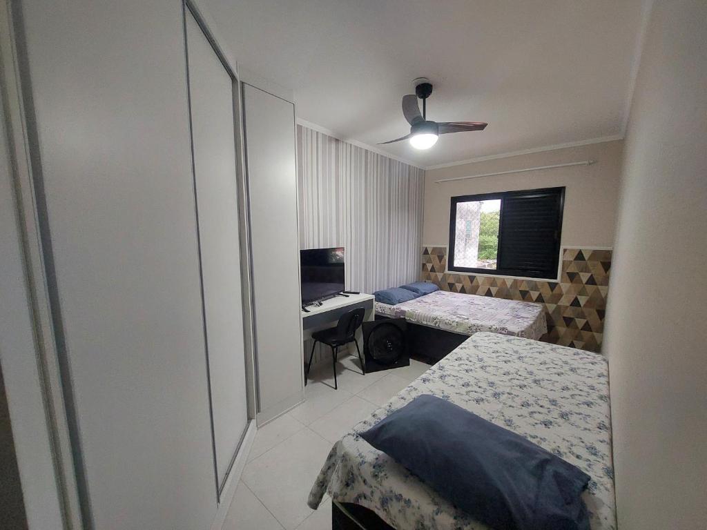 a bedroom with two beds and a desk with a computer at Apto Centro Bertioga (800 metros da praia) in Bertioga