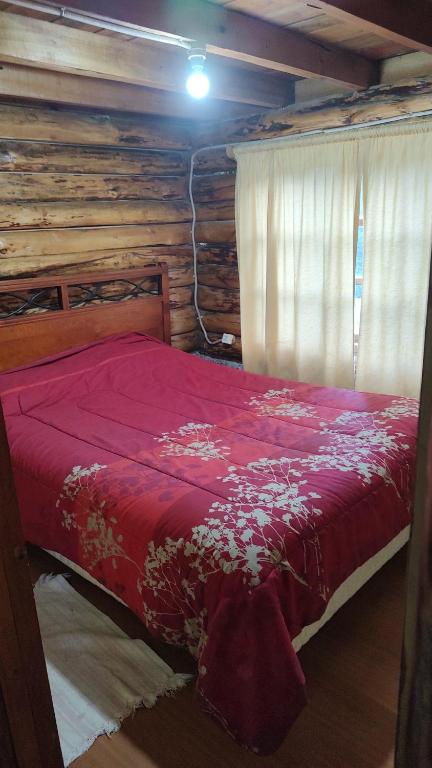 a bedroom with a red bed in a log cabin at Cabaña Los Nietos in Futaleufú