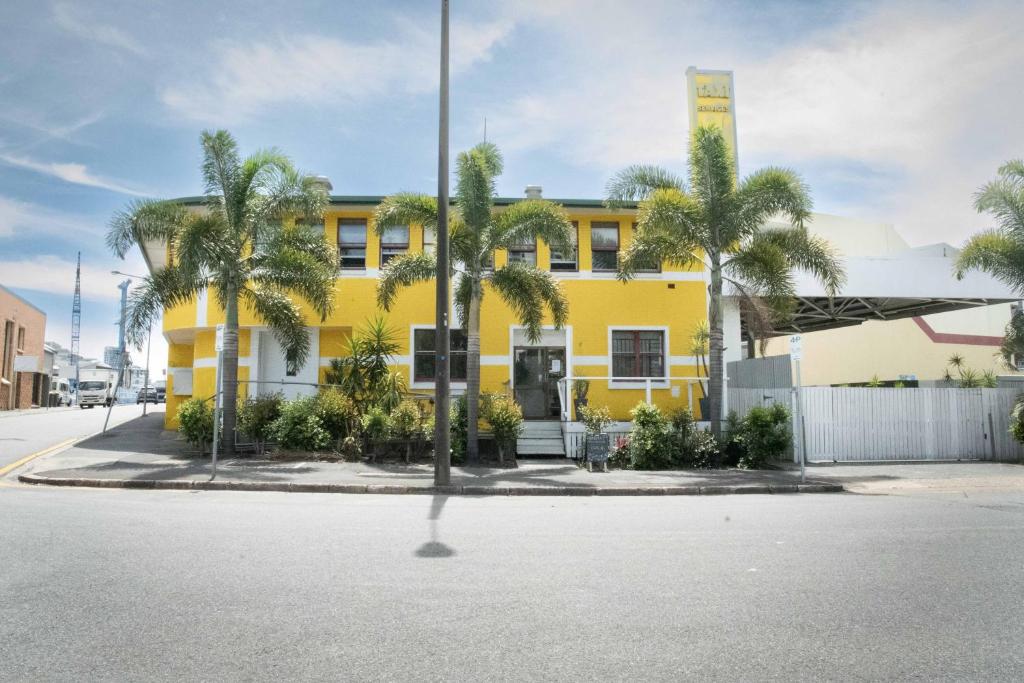 a yellow building with palm trees in front of it at Habitat Backpackers in Brisbane
