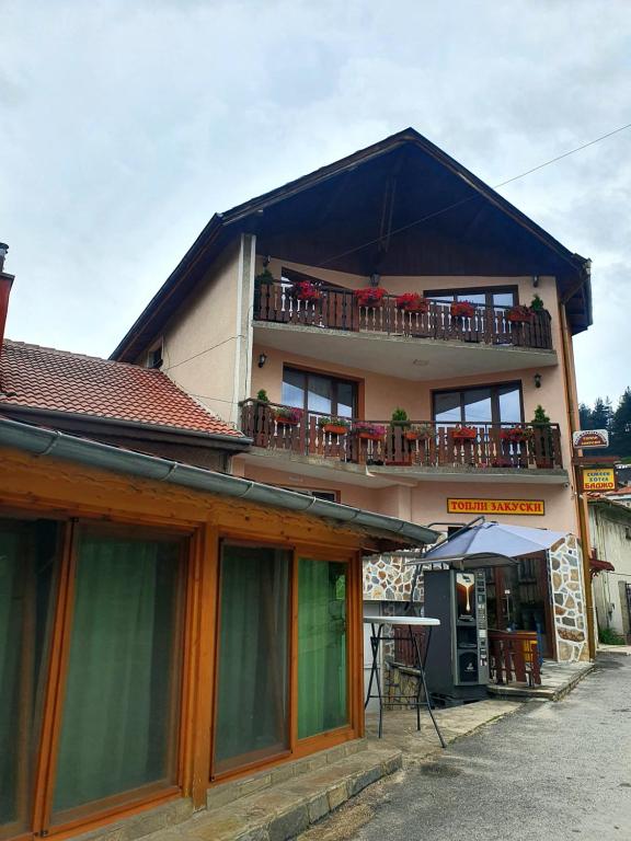 ein Gebäude mit einem Balkon mit Tischen und Stühlen in der Unterkunft Къща за гости с механа Баджо in Dospat