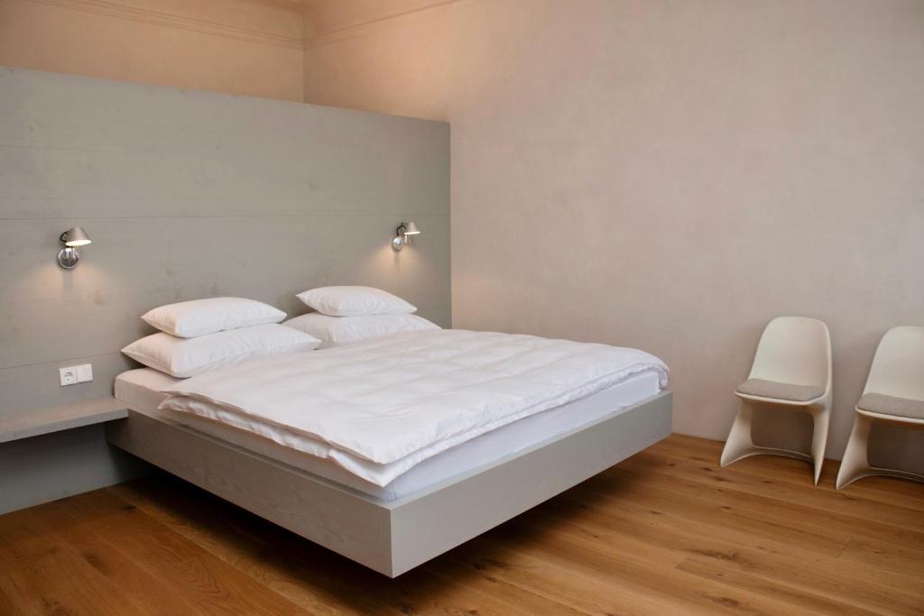 una camera da letto con un letto con lenzuola bianche e due sedie di Der Pfarrhof a Hartberg