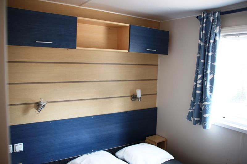 a bedroom with a blue headboard and a window at Camping La Prévoté in Saint-Hilaire-de-Riez