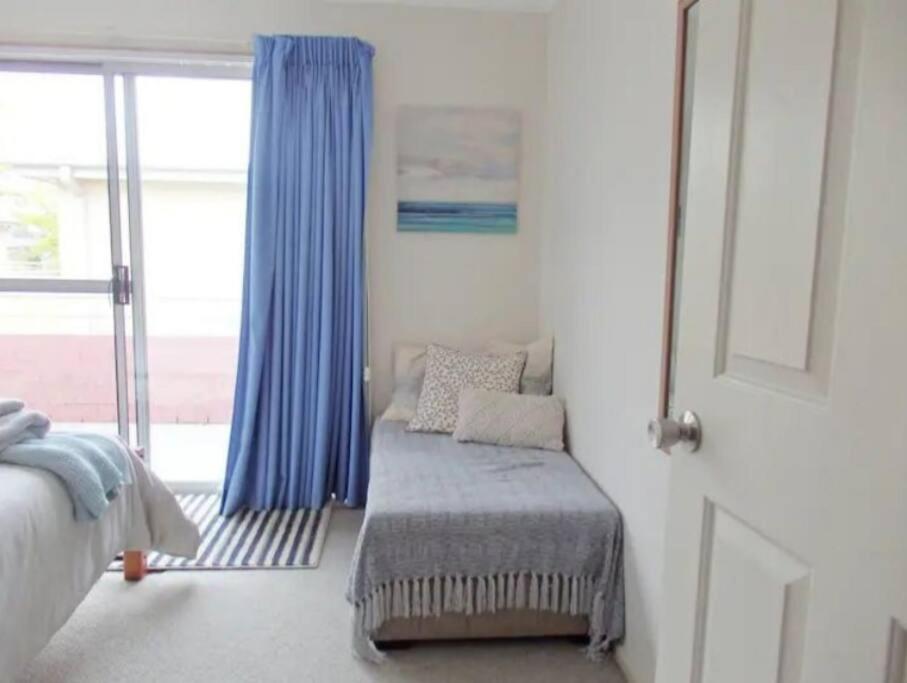 a bedroom with a chair and a window with blue curtains at Bec's Beach House Getaway in Batemans Bay