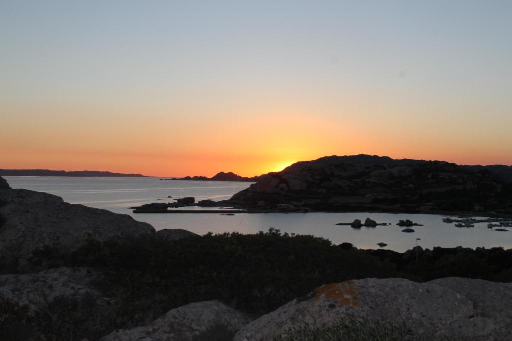 una puesta de sol sobre un cuerpo de agua con rocas en A Punta Tegge il mare la spiaggia il tramonto bilocale en La Maddalena