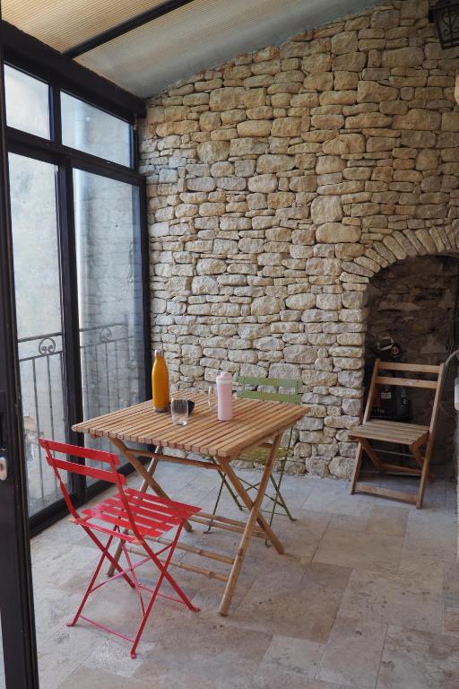 - une table en bois et 2 chaises rouges dans une chambre dotée d'un mur en pierre dans l'établissement maison Jonquière millet, à Jonquières