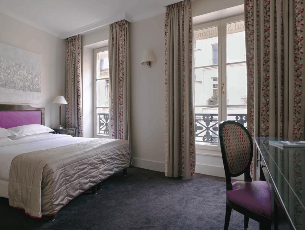 a bedroom with a bed and two windows and a chair at Hotel Royal Saint Honore Paris Louvre in Paris