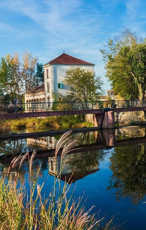 un pont sur une rivière avec un bâtiment en arrière-plan dans l'établissement La Ferblanterie, à Rambervillers