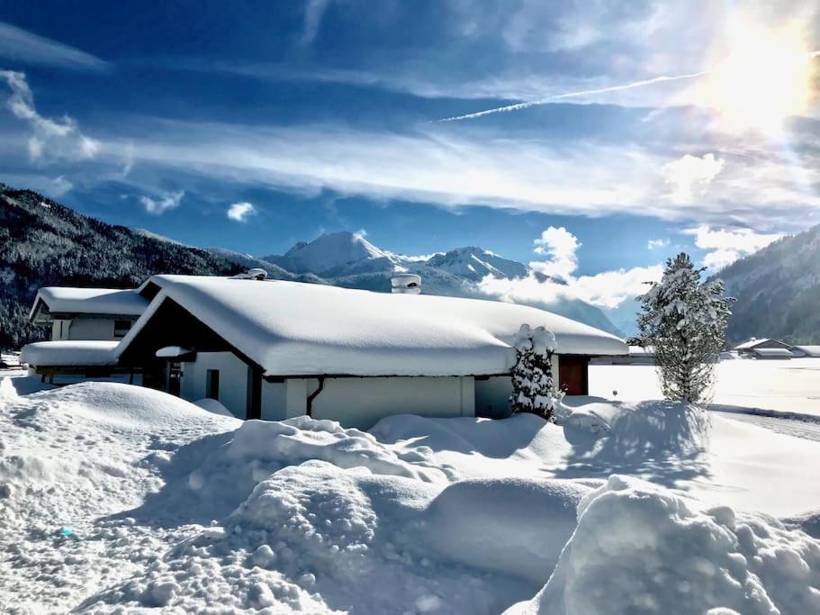 una casa cubierta de nieve con montañas en el fondo en Das Ferienhaus in Achenkirch en Achenkirch