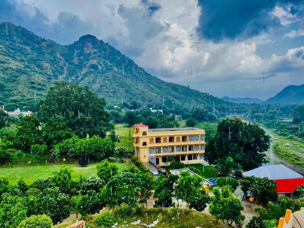 Udai Valley Resort- Top Rated Resort in Udaipur with mountain view في أودايبور: مبنى في حقل مع جبال في الخلف