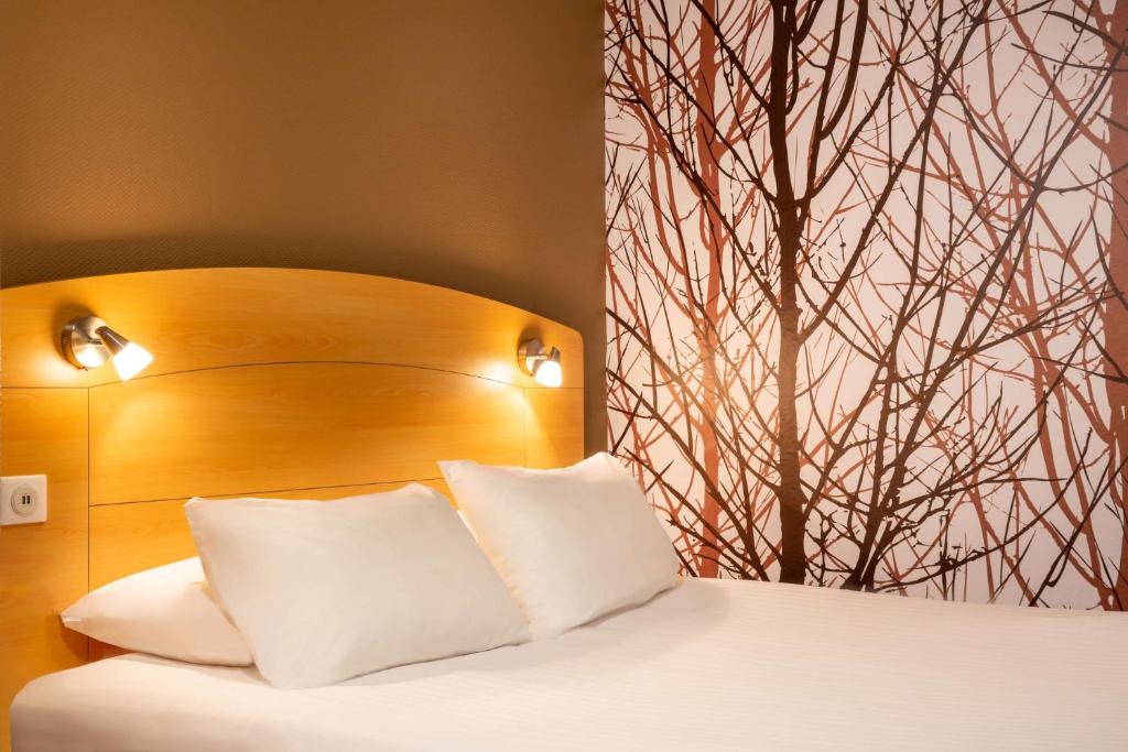 a bed with a wooden headboard and white pillows at Sure Hotel by Best Western Plaisir in Plaisir