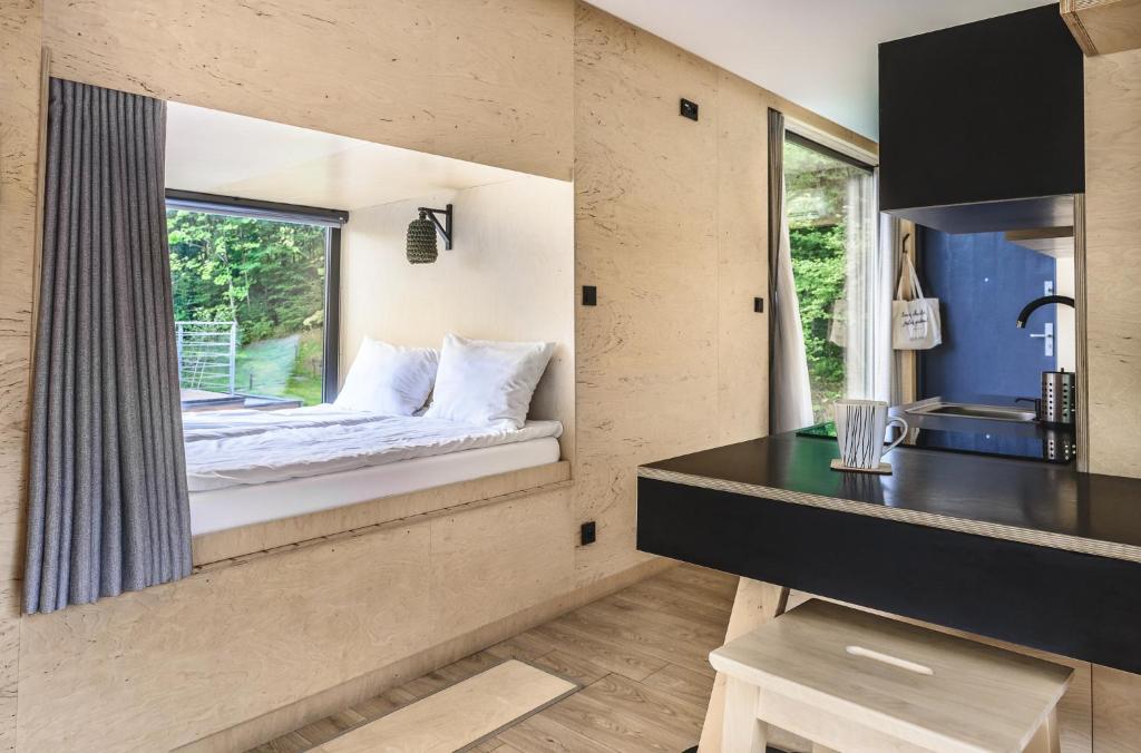 Cozy bunk-style bed nook beside a small table and kitchenette, curtain partially drawn toward forest view.