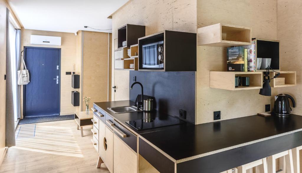 Bright kitchenette from angle, black countertops, microwave, open shelving, breakfast bar with stools.