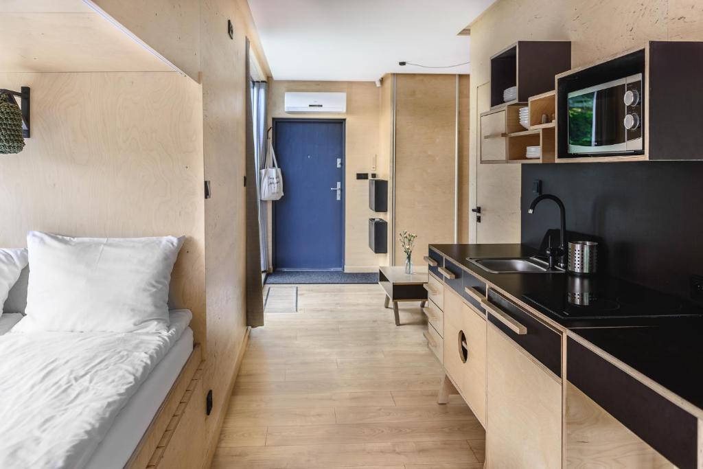 Hallway view of studio interior with bed, kitchenette, blue entry door, and wood flooring.