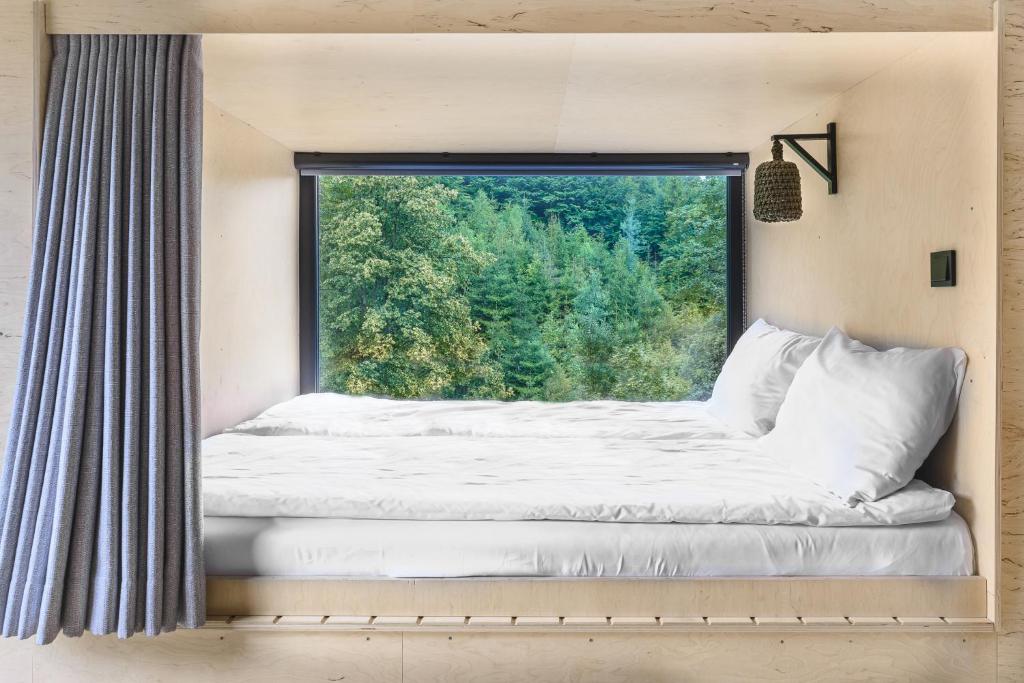 Built-in bed framed by a large window with pillows, offering a serene view of trees outside.