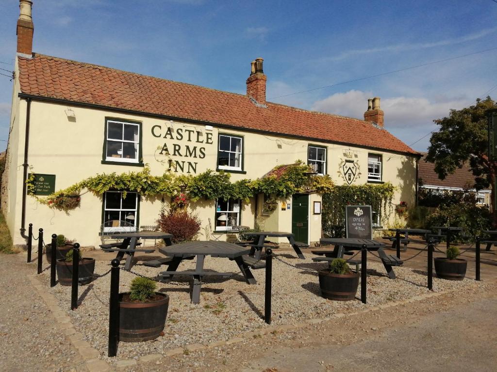 un edificio con mesas de picnic delante de él en The Castle Arms Inn, en Bedale