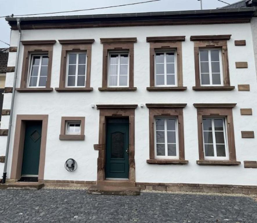 ein weißes Haus mit grüner Tür und Fenstern in der Unterkunft Feriendomizil im Saarschleifenland - Ferienhaus Gätschenberger in Mettlach