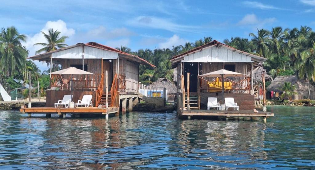 dos casas en el agua con sillas y sombrillas en Cabañas sobre el mar en San Blas Narasgandub., en Nusatupo