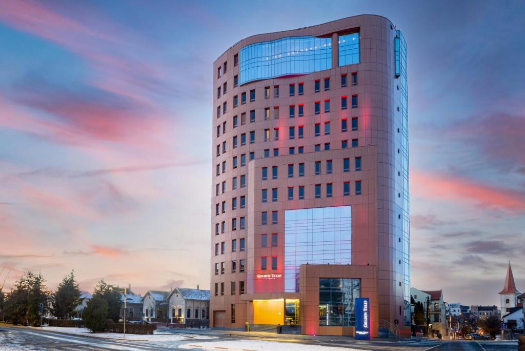 un edificio alto de color rojo con una puesta de sol en el fondo en Hotel Golden Tulip Ana Tower Sibiu, en Sibiu