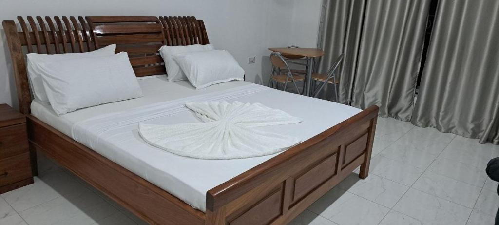1 cama con cabecero de madera y sábanas y almohadas blancas en Kingson Hotel, en Dar es Salaam