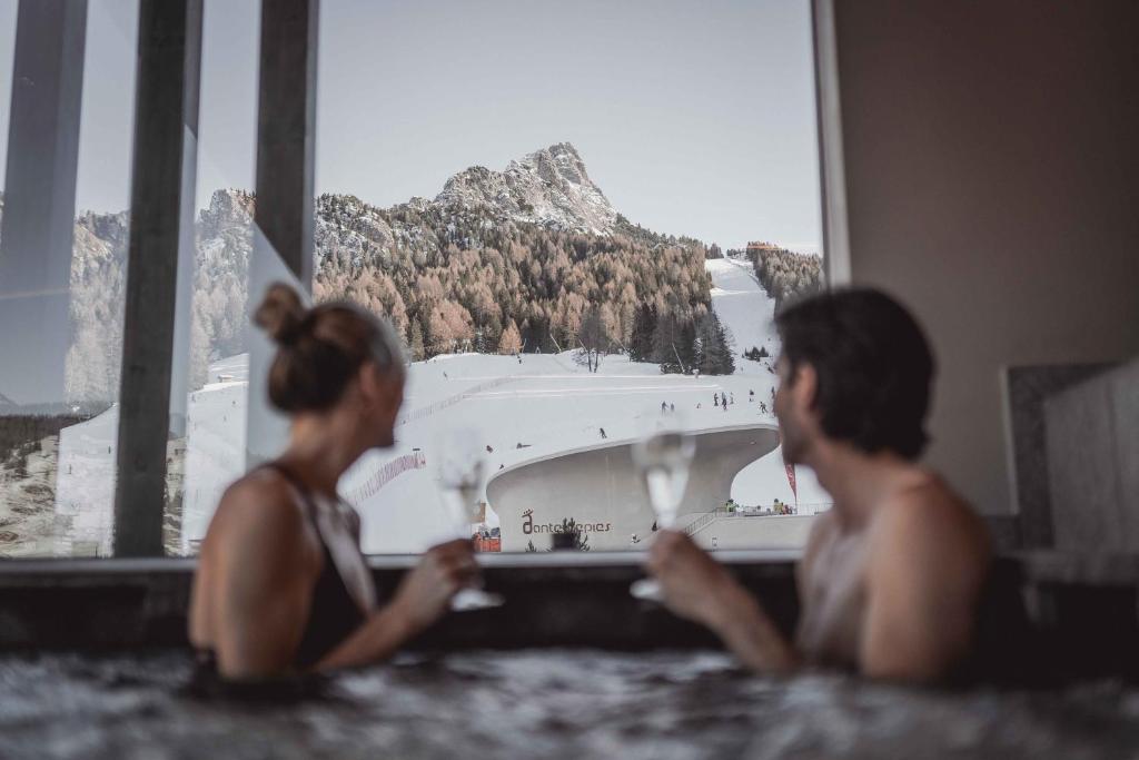 Due donne sedute in una vasca da bagno che guardano fuori dalla finestra di Hotel Continental a Selva di Val Gardena